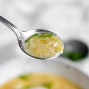 A spoon of egg drop soup with green onions on top.
