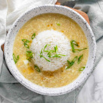 Egg drop soup in a bowl with a rounded ball of rice in the center and green onions on top.
