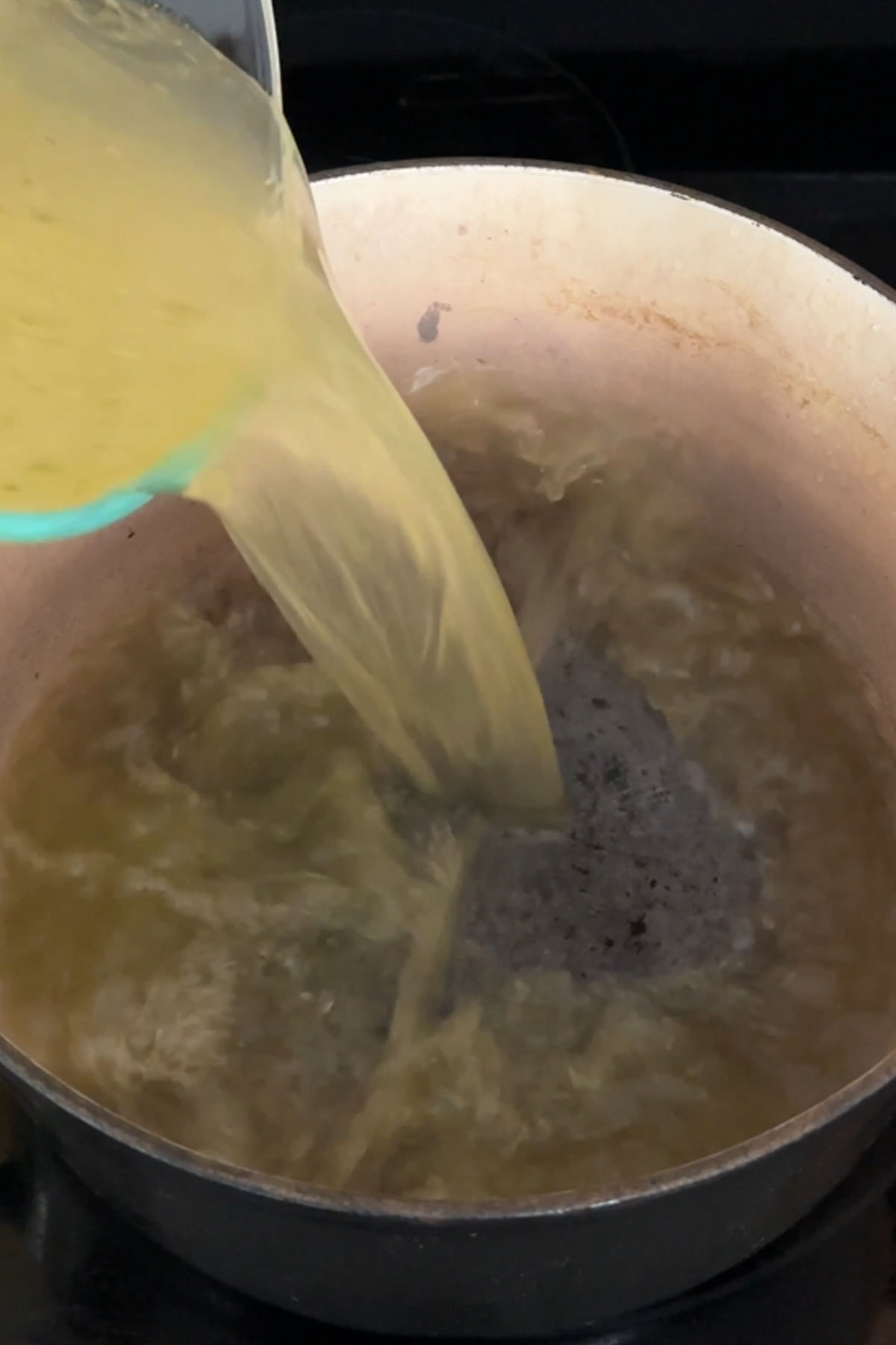 Broth is poured into a large enameled cast iron dutch oven.