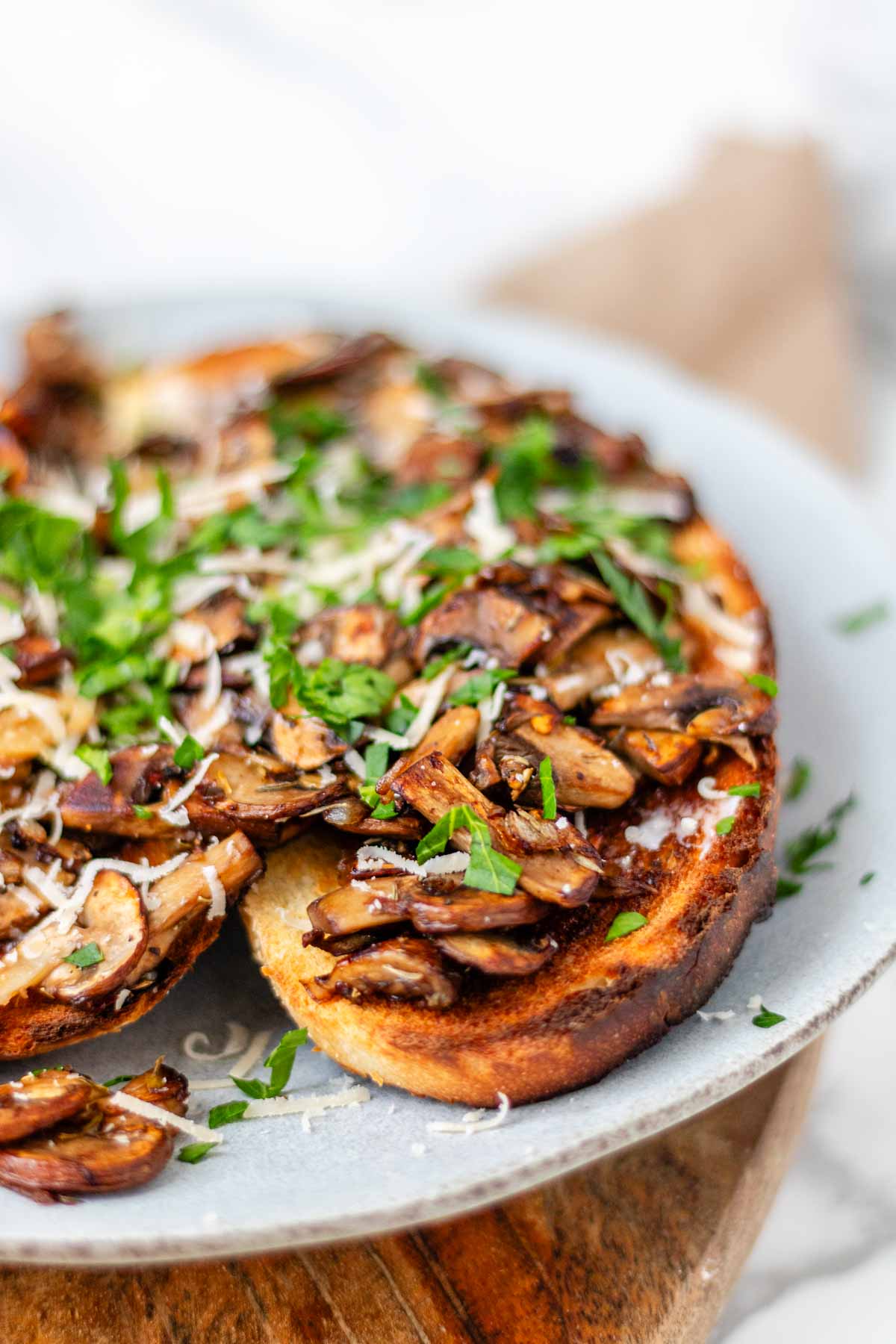 Toast on a plate topped with mushrooms, cheese, and parsley.