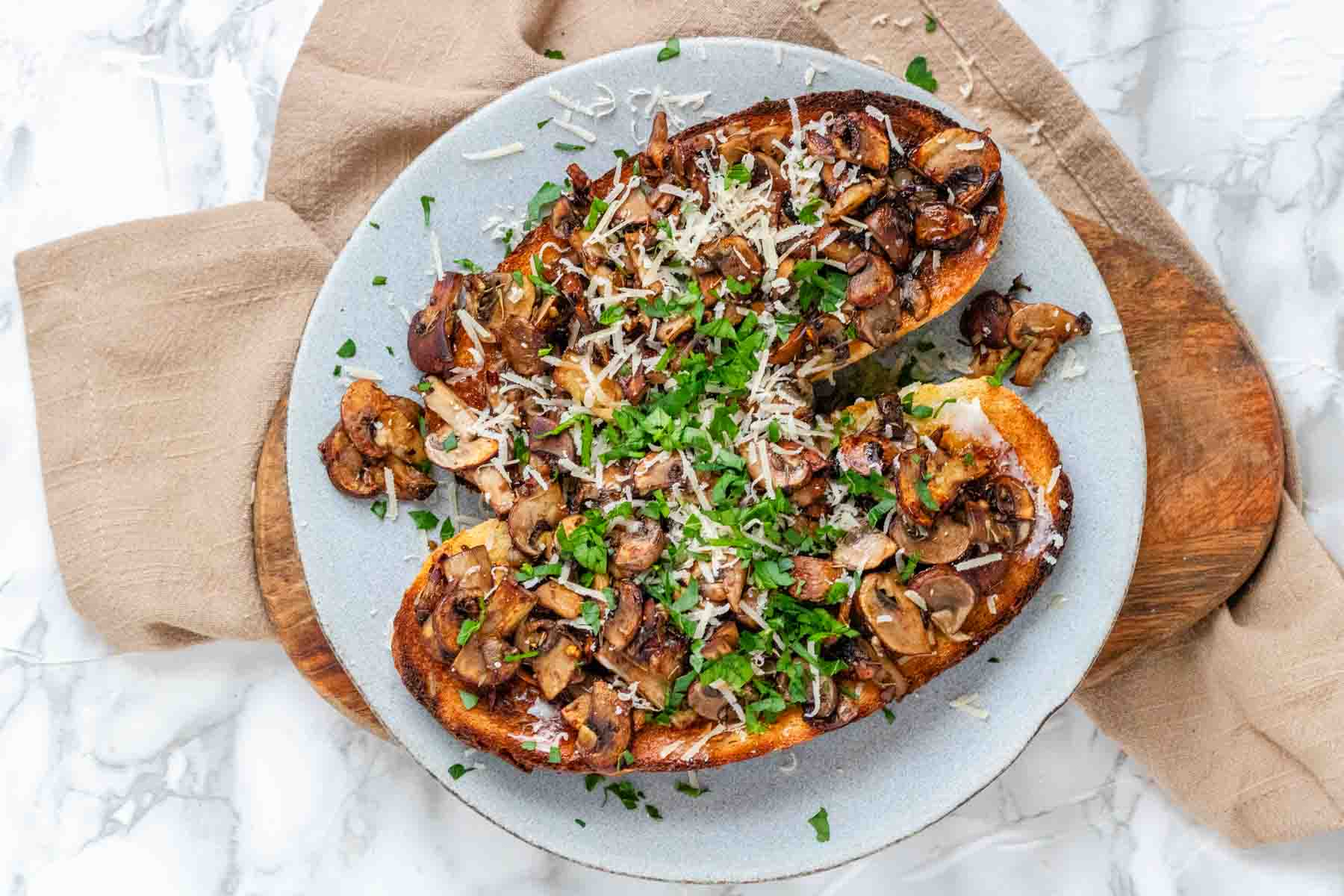 Toast on a plate topped with mushrooms, cheese, and parsley.