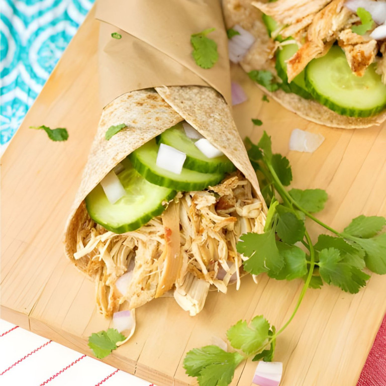 A wrap with chicken, cucumbers, and onion in it.