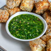 Bright green chimichurri sauce in a bowl surrounded by air-fried breaded paneer.