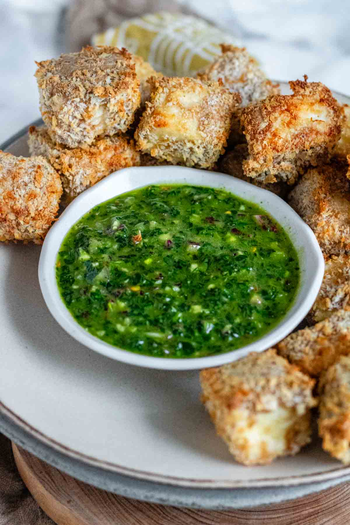 Bright green chimichurri sauce in a bowl surrounded by air-fried breaded paneer.