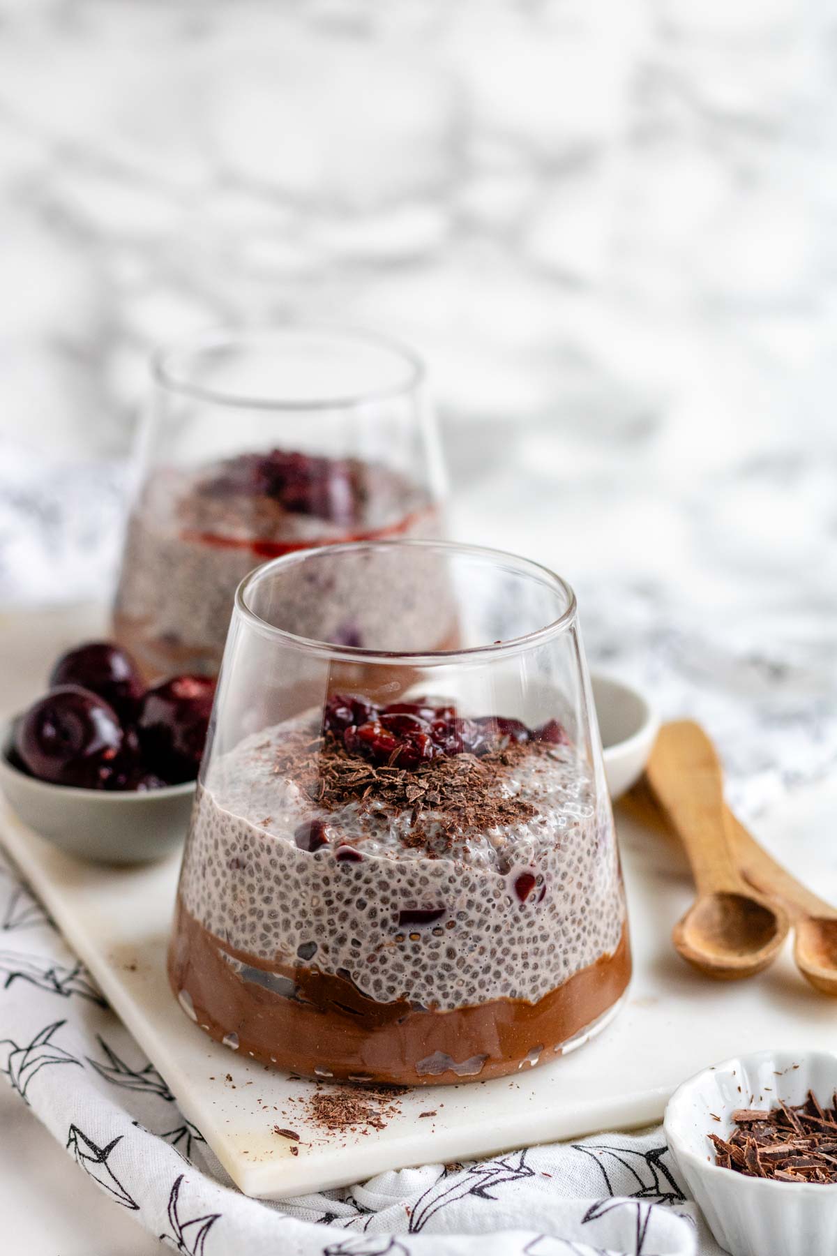A glass with chocolate pudding on the bottom topped with chia pudding, cherries, and chocolate shavings.