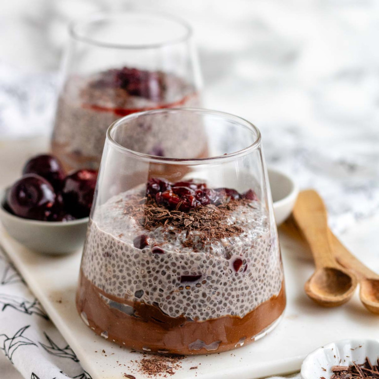 A glass with chocolate pudding on the bottom topped with chia pudding, cherries, and chocolate shavings.