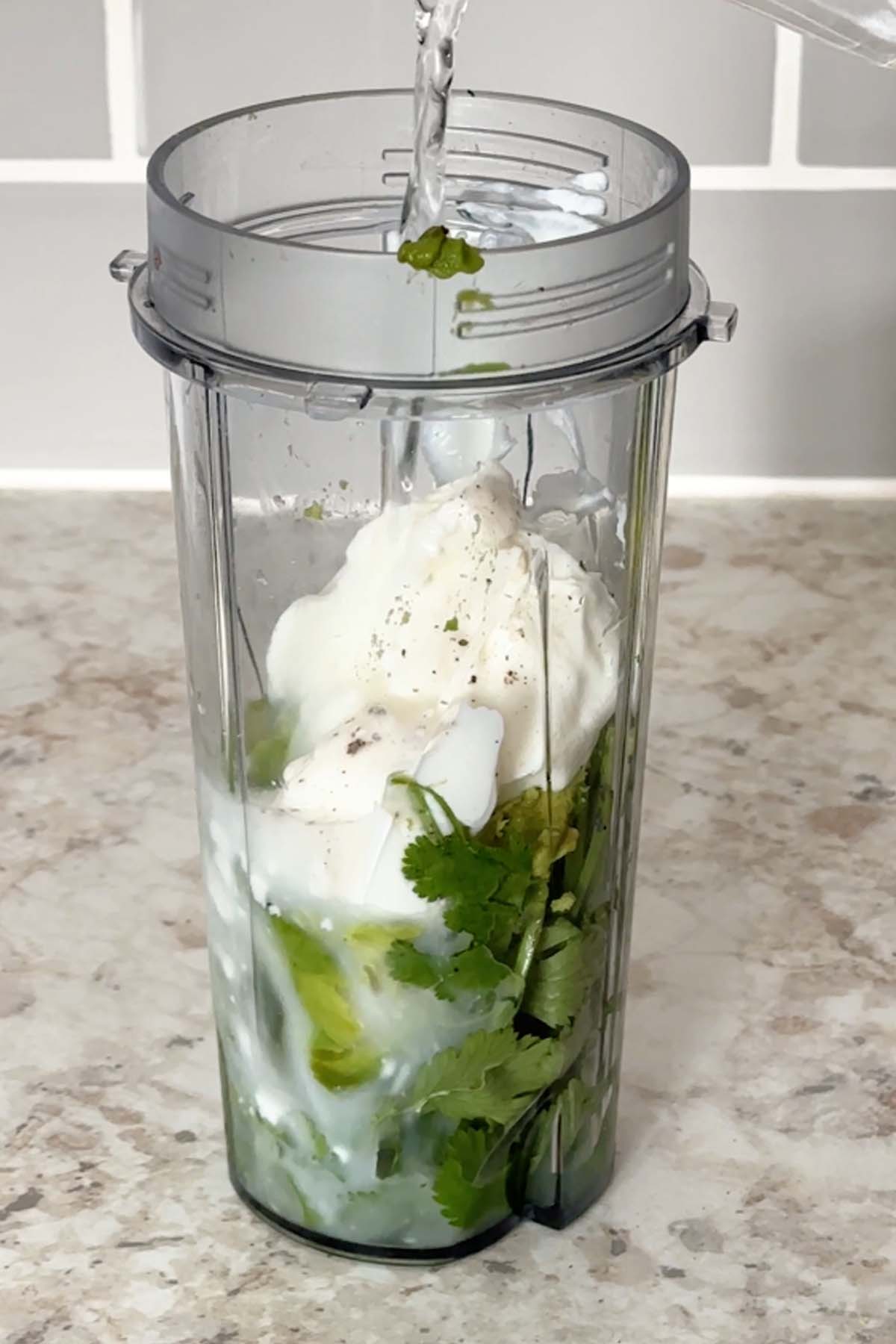 Cilantro, yogurt, lime juice, and avocado in a blender cup.