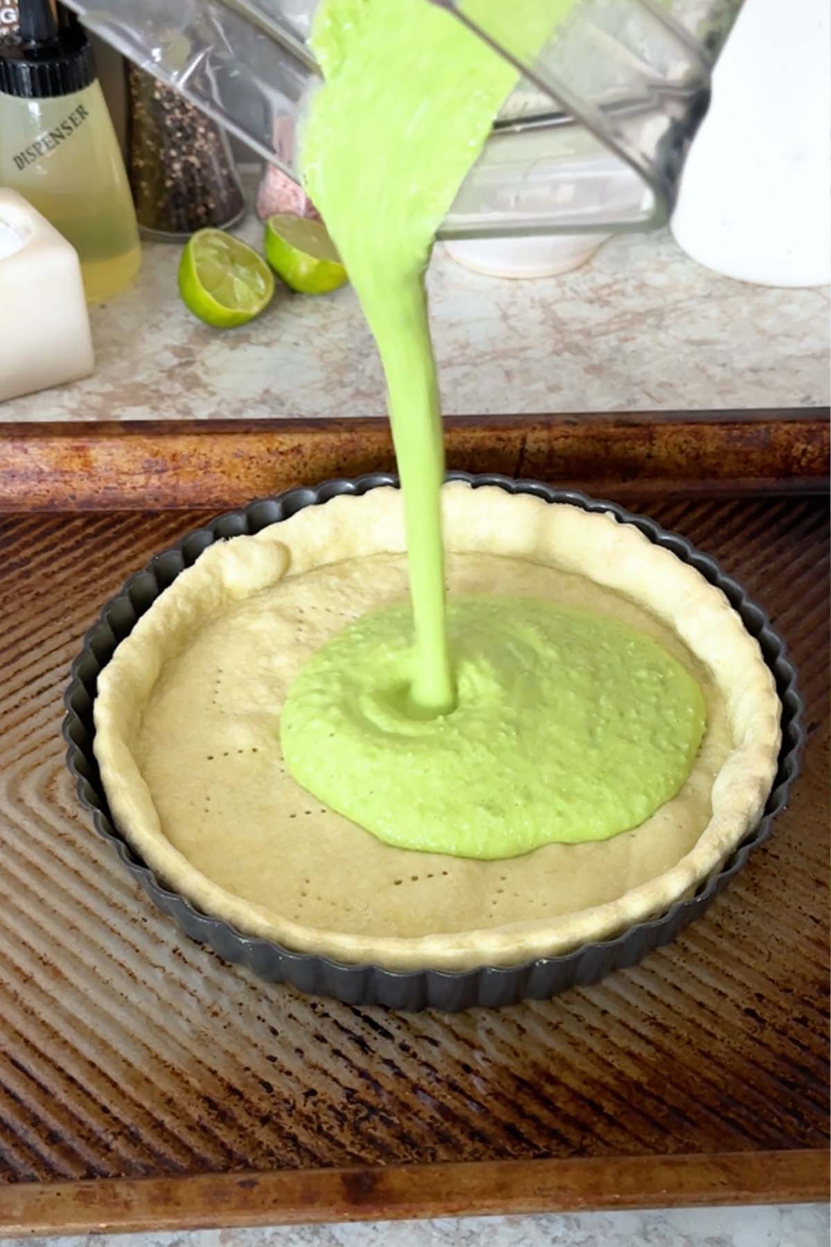 A green quiche filling is poured into a baked pie crust.