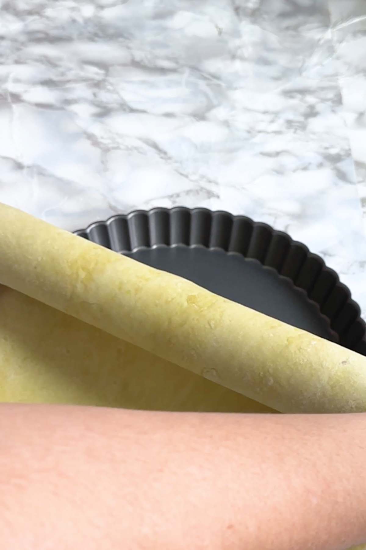 Pie dough is rolled off of a rolling pin into a tart pan.