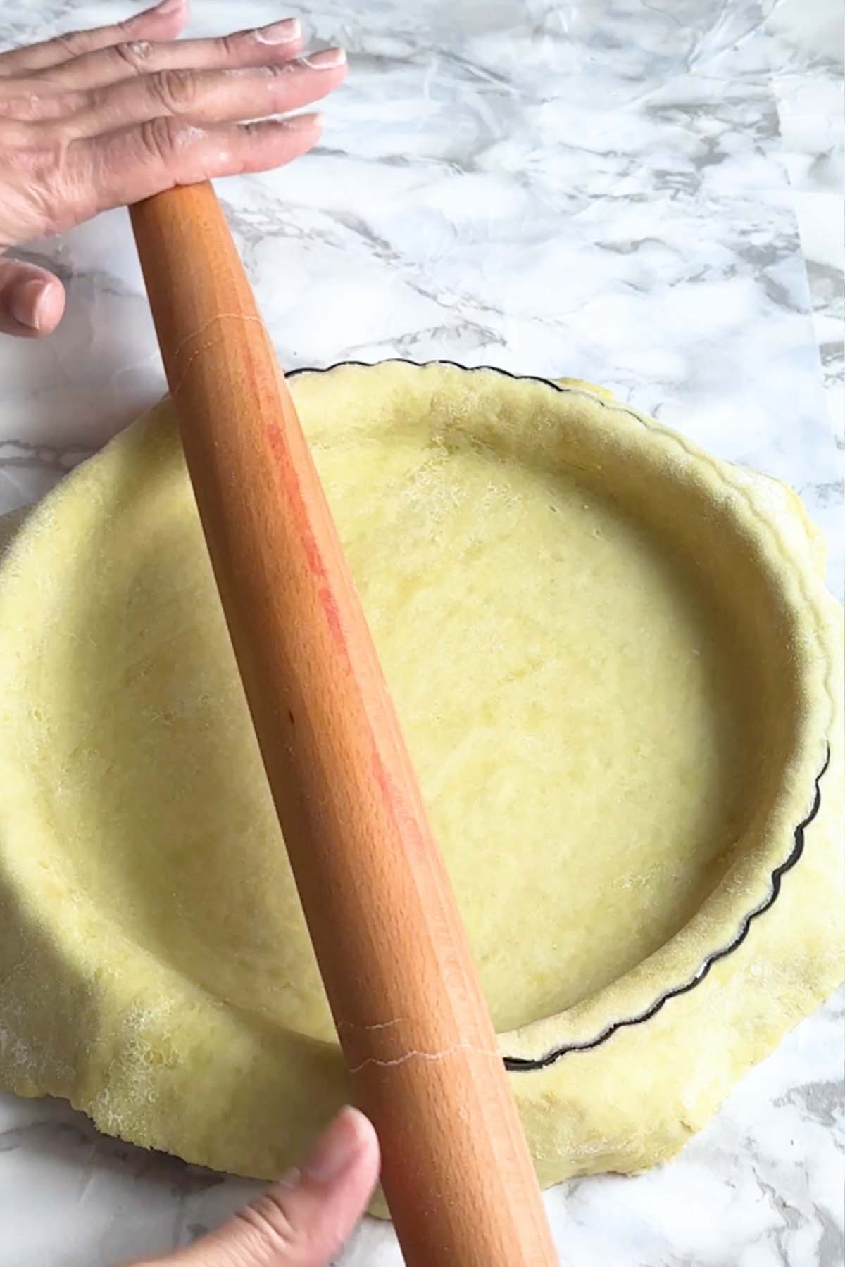 Excess pie dough is cut by rolling a rolling pin on the edges of a pie tin.