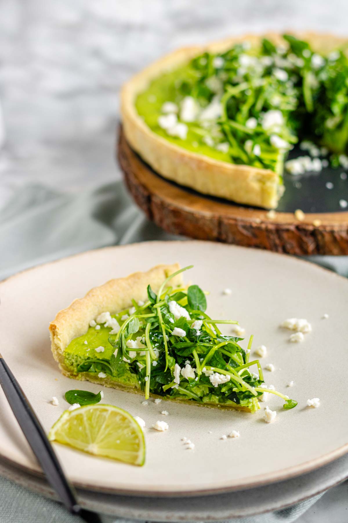 Quiche on a plate with a green filling topped with pea shoots and feta cheese.