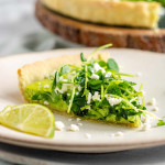 Quiche on a plate with a green filling topped with pea shoots and feta cheese.