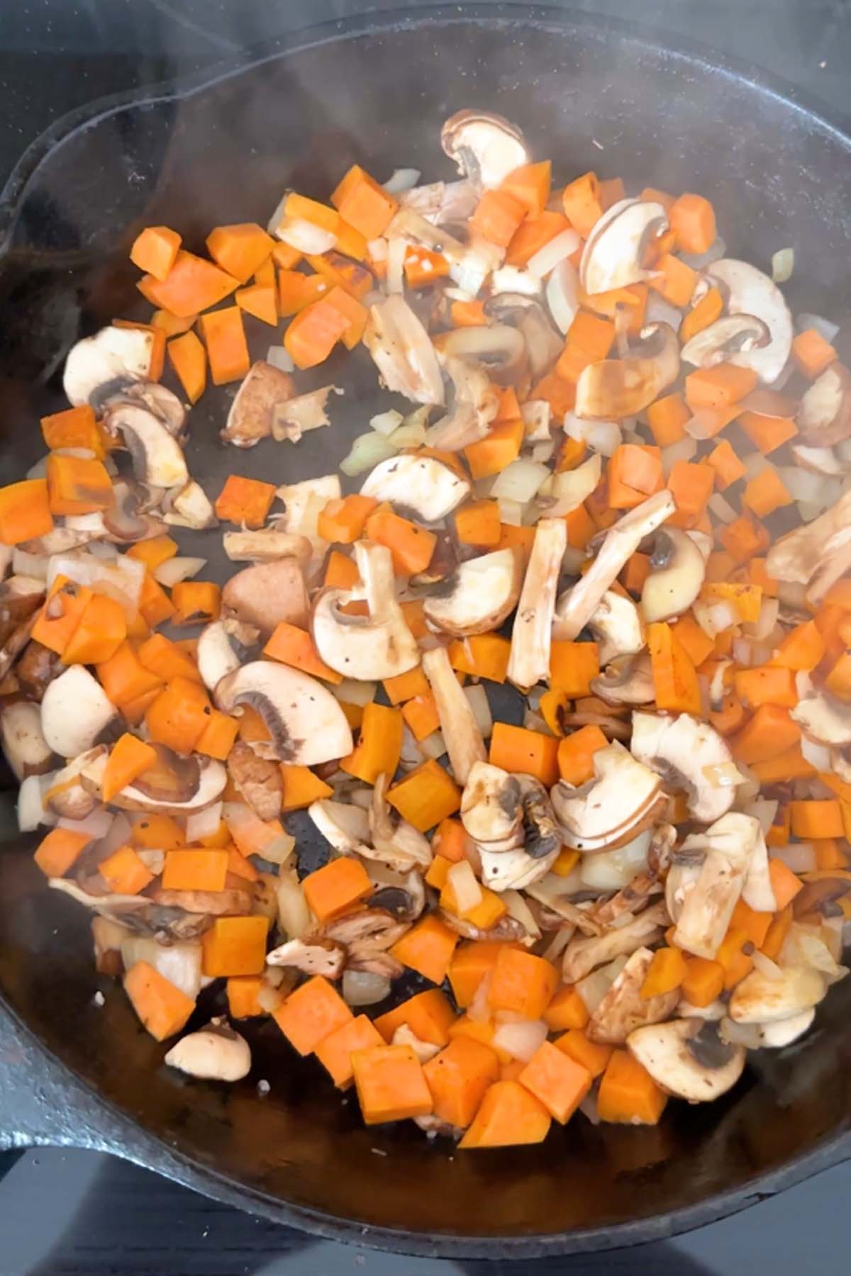 Cubed sweet potato and sliced mushrooms in a cast iron skillet.