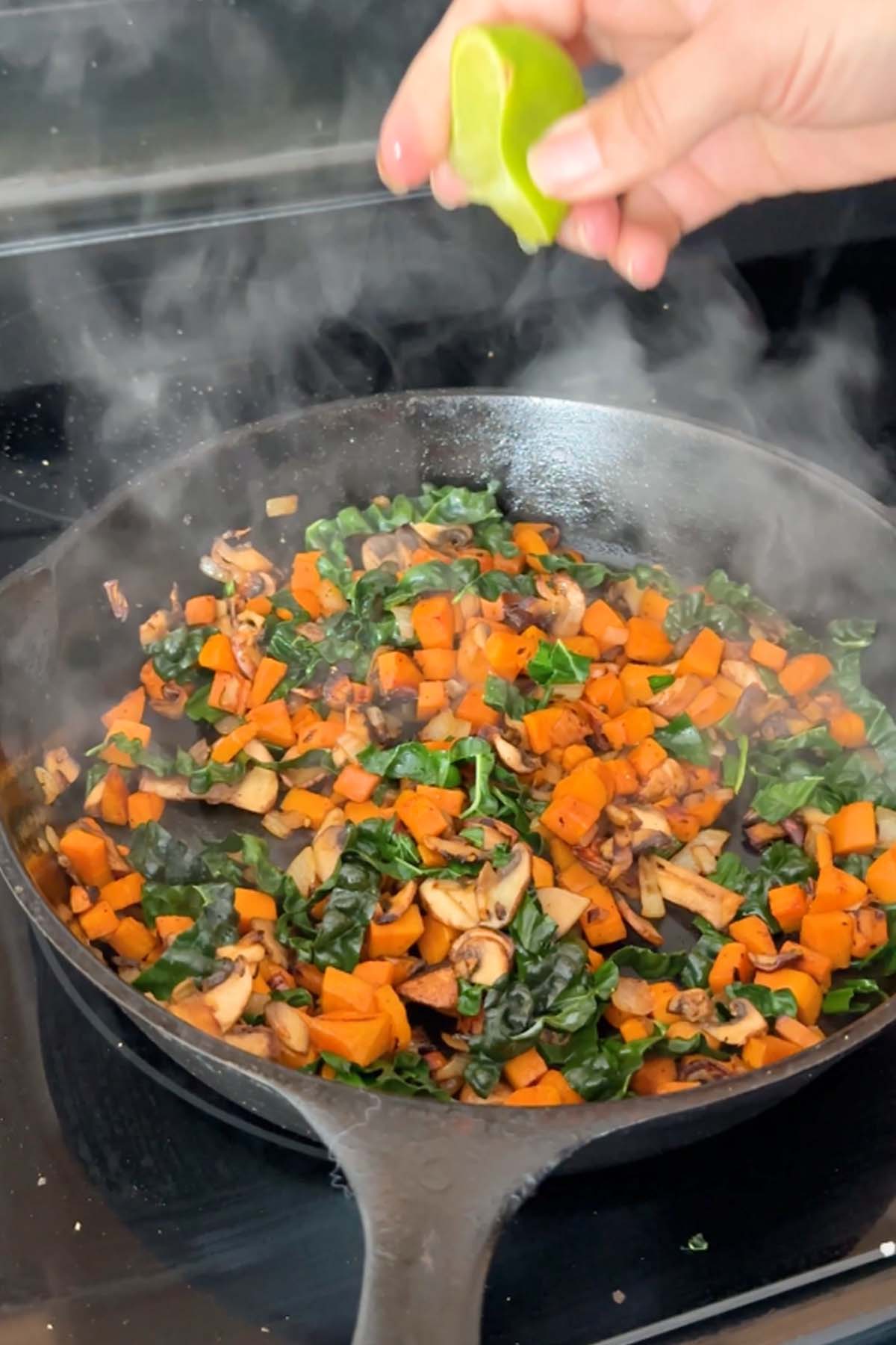 Lime juice squeezed onto cubed sweet potato, kale, and sliced mushrooms in a cast iron skillet.