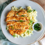 Sliced breaded chicken on a plate with rice and a small bowl of green onions.