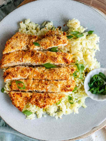 Sliced breaded chicken on a plate with rice and a small bowl of green onions.