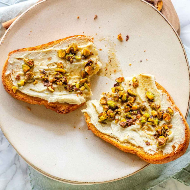 A halved slice of toast on a plate with cream cheese and nuts on it.