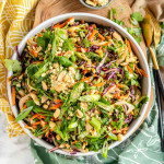 A bowl with a shredded colorful salad topped with green onions, cilantro, and chopped peanuts.