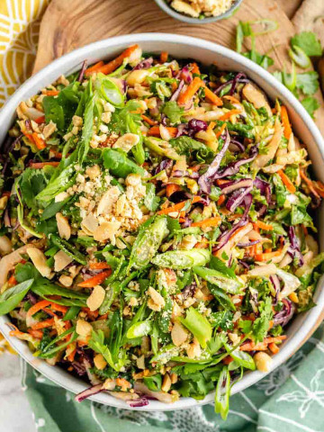 A bowl with a shredded colorful salad topped with green onions, cilantro, and chopped peanuts.