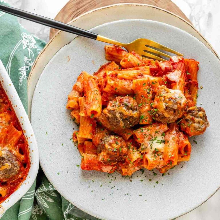 Pasta and meatballs on a plate wit a fork with cheese and parsley on top.