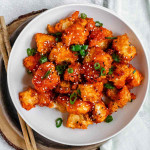 Breaded and sauce covered cauliflower in a bowl, with green onions on top.