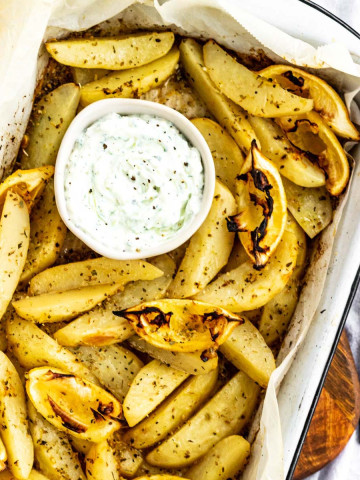 Potatoes in a roasting dish with a bowl of white dip.