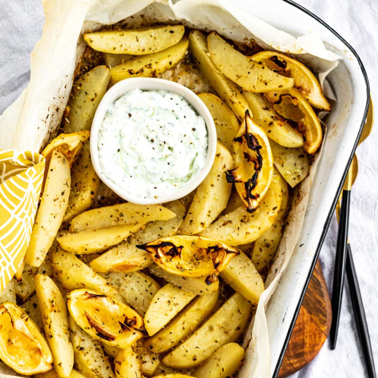 Potatoes in a roasting dish with a bowl of white dip.