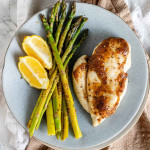A chicken breast, asparagus, and lemon wedges on a plate.