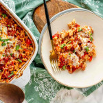A casserole dish and plate with a fork each containing a rice casserole recipe covered in cheese and parsley.