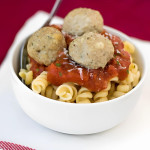 Pasta in a bowl topped with red sauce and three meatballs.