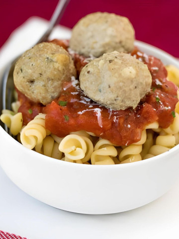 Pasta in a bowl topped with red sauce and three meatballs.