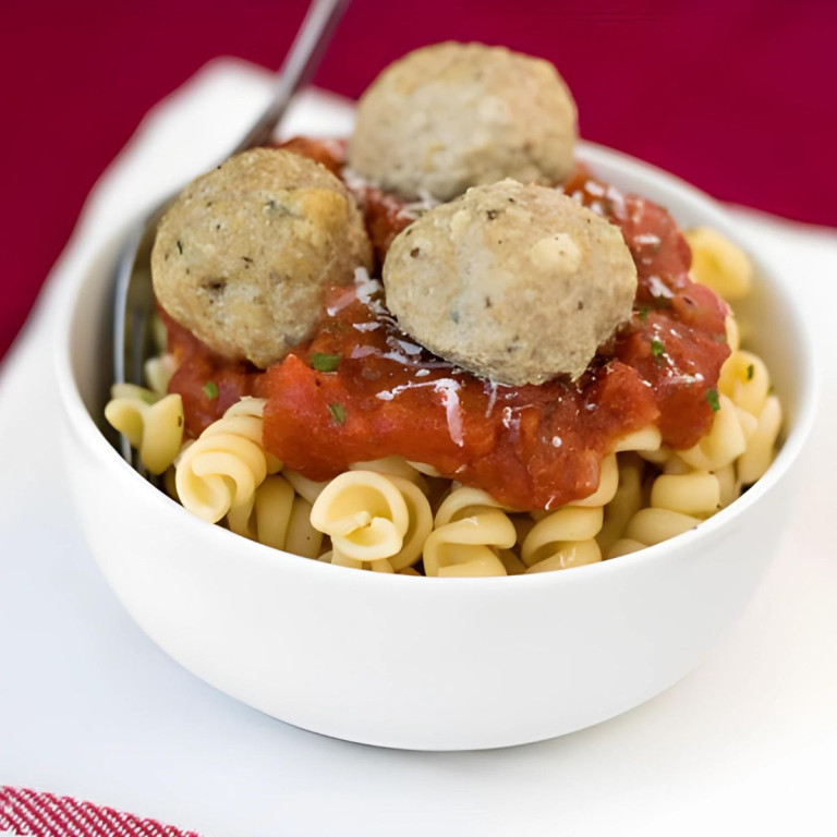 Pasta in a bowl topped with red sauce and three meatballs.