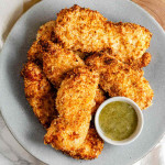 Breaded chicken strips on a plate with a bowl of dip.