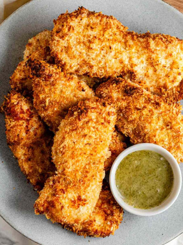 Breaded chicken strips on a plate with a bowl of dip.