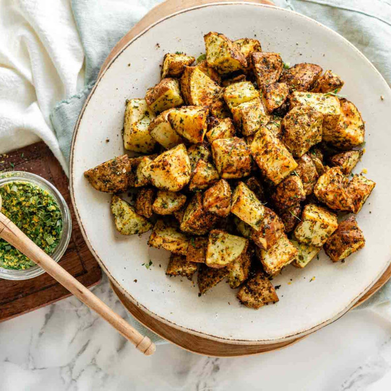 Crispy cubed potatoes on a plate, coated in a seasoning mix.