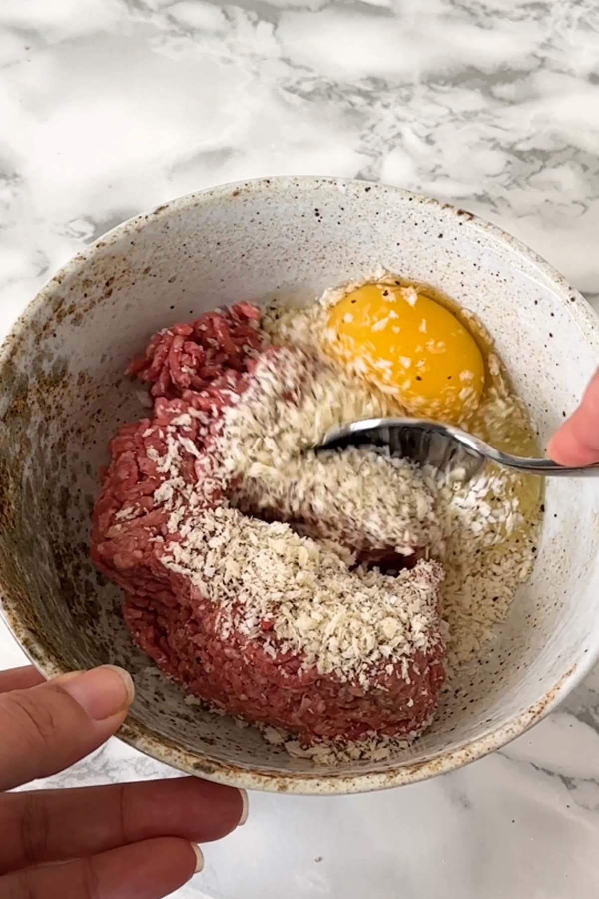 A spoon mixes ground beef with breadcrumbs and egg.