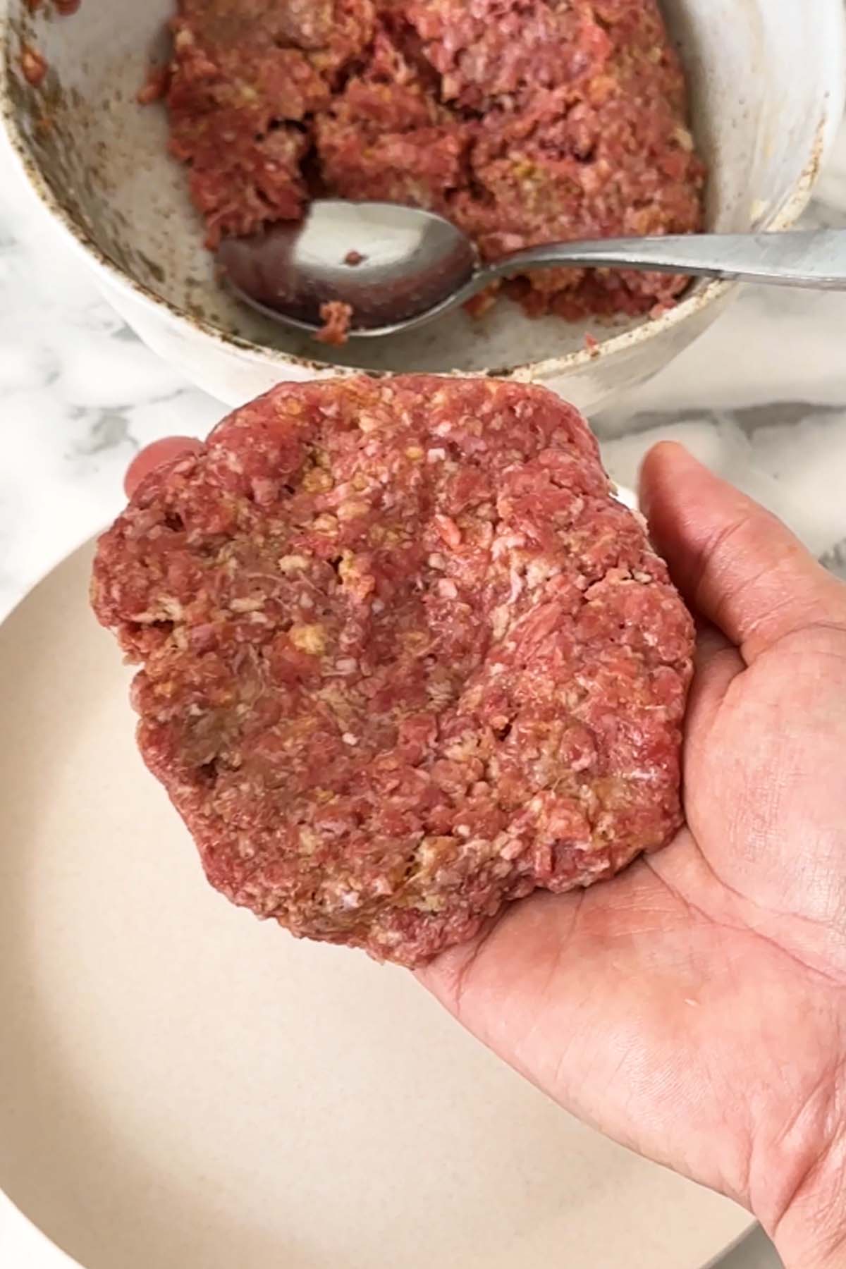 A hand holds a formed burger patty.