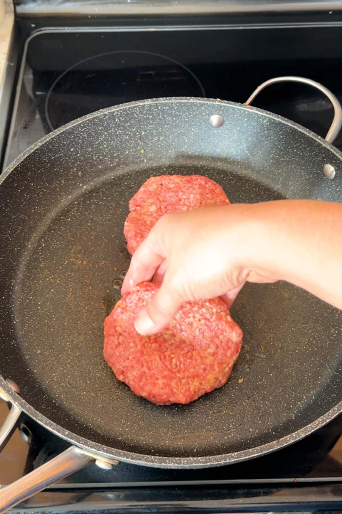 Raw burger patties placed in a skillet.