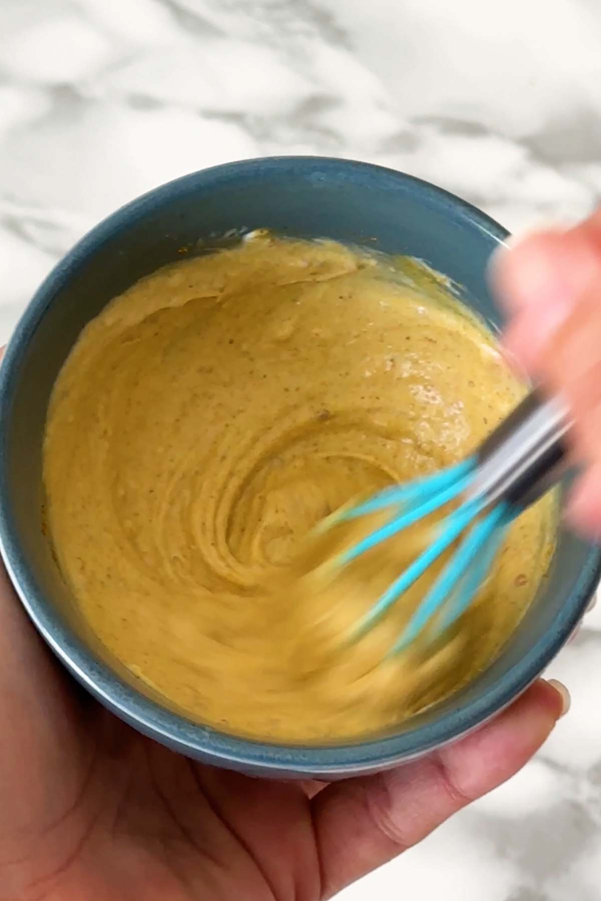 Yellow sauce is whisked in a blue bowl.