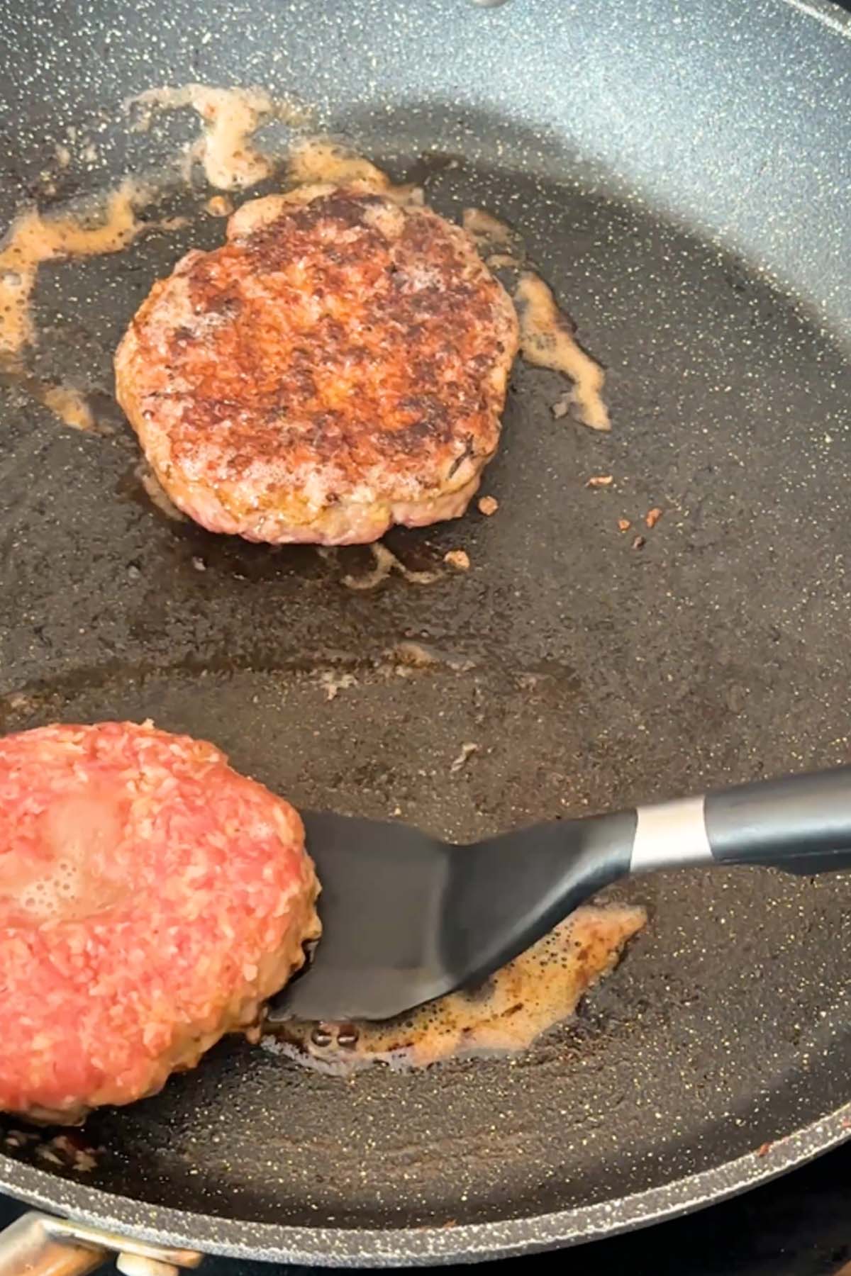 Burgers cook in a skillet.
