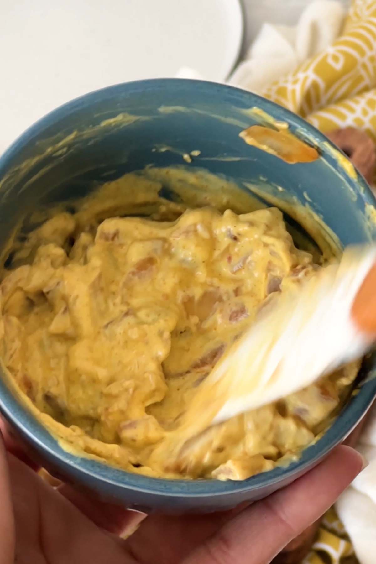 A chunky yellow sauce is stirred in a blue bowl.