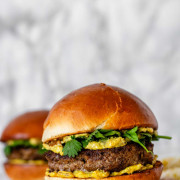 A burger with yellow sauce and cilantro leaves.
