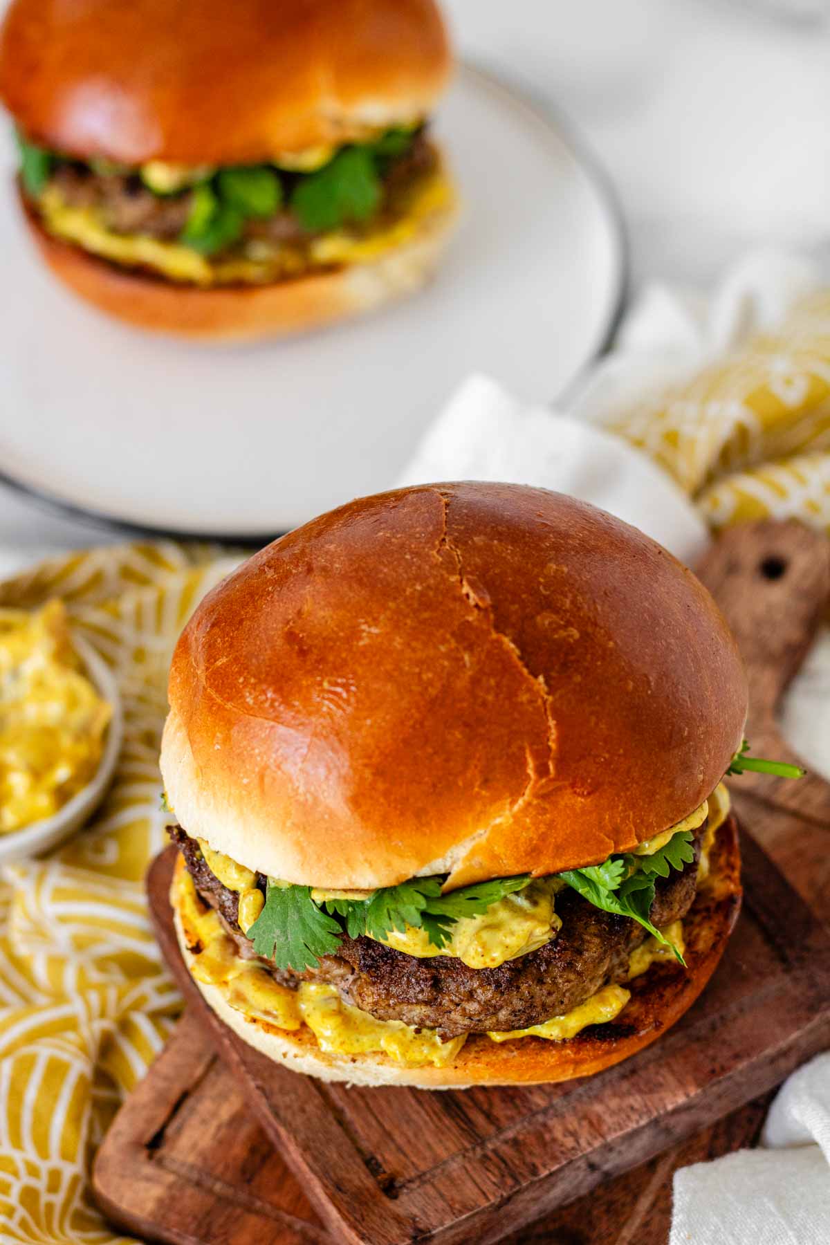 A burger with yellow sauce and cilantro leaves.