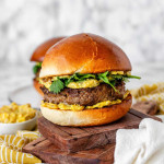 A burger with yellow sauce and cilantro leaves.