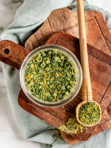 A seasoning mix of yellow and green in a jar with a wooden spoon full of seasoning mix beside it.