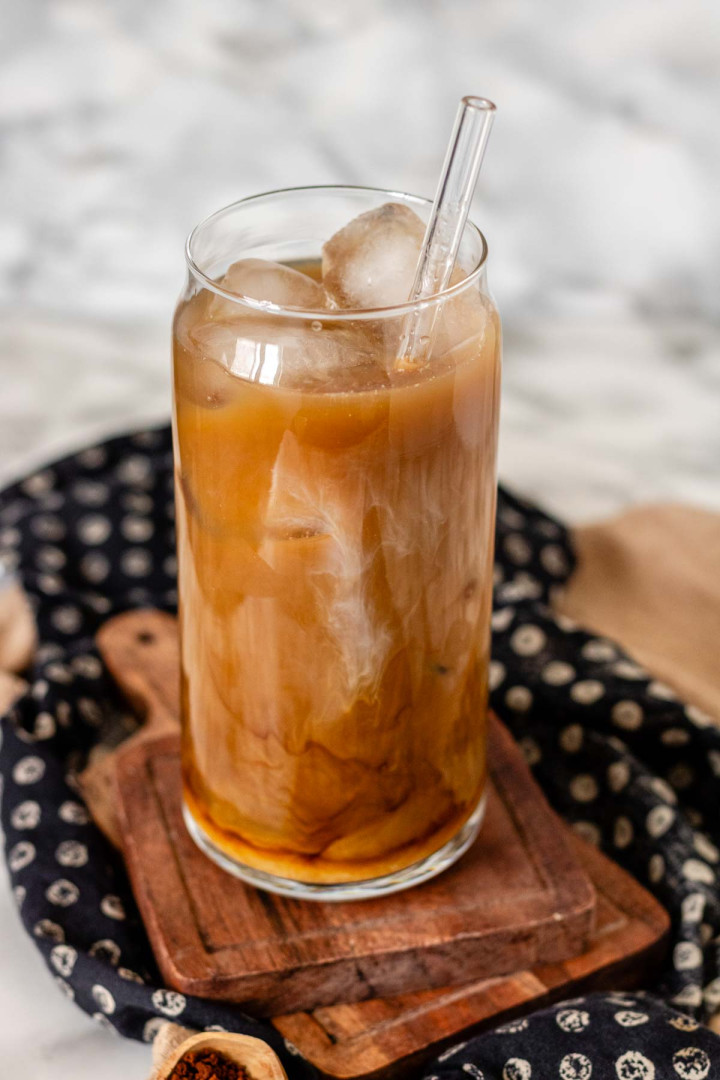 Light-colored coffee in a glass with a straw and ice cubes.