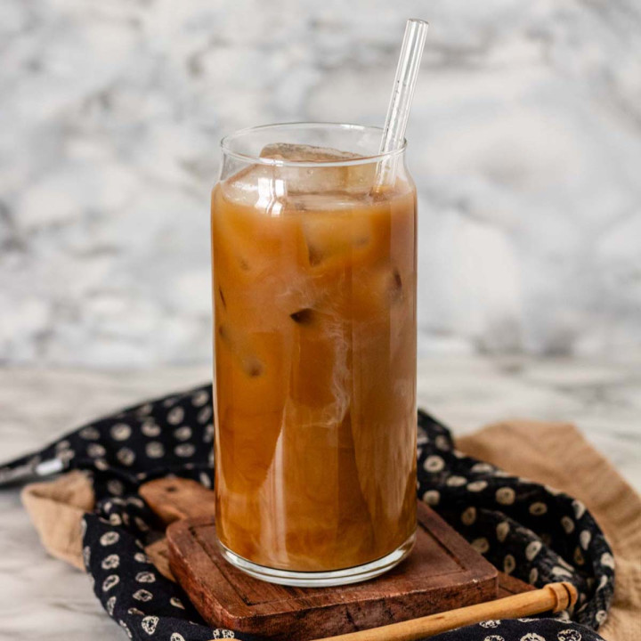 Light-colored coffee in a glass with a straw and ice cubes.