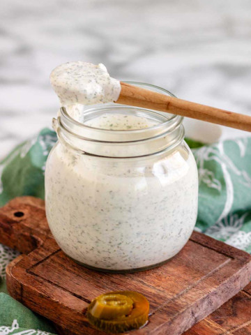 A creamy white dressing in a jar with a spoon of dressing laying across the top of the jar.