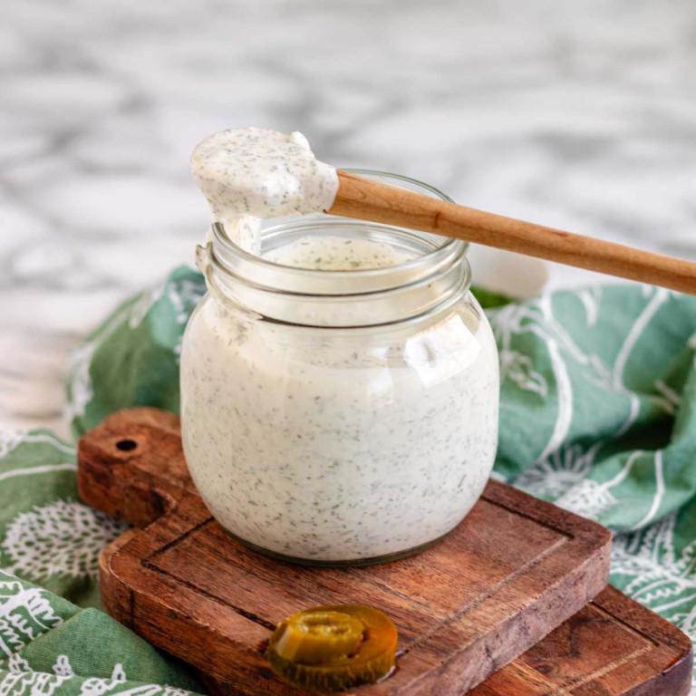 A creamy white dressing in a jar with a spoon of dressing laying across the top of the jar.