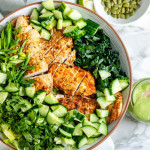 Greens in a bowl with cucumbers and sliced chicken.